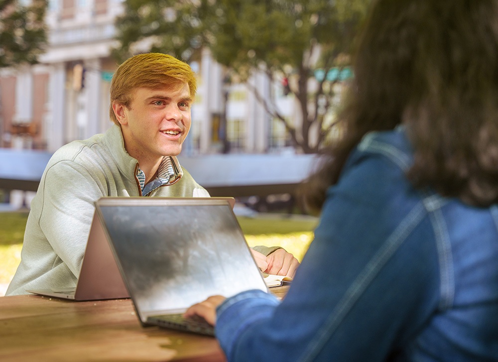 Two students sitting and discussing with laptops