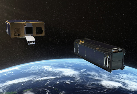 An artist's concept of two satellites in space, with one deploying a large, reflective solar sail. Earth is visible in the background.