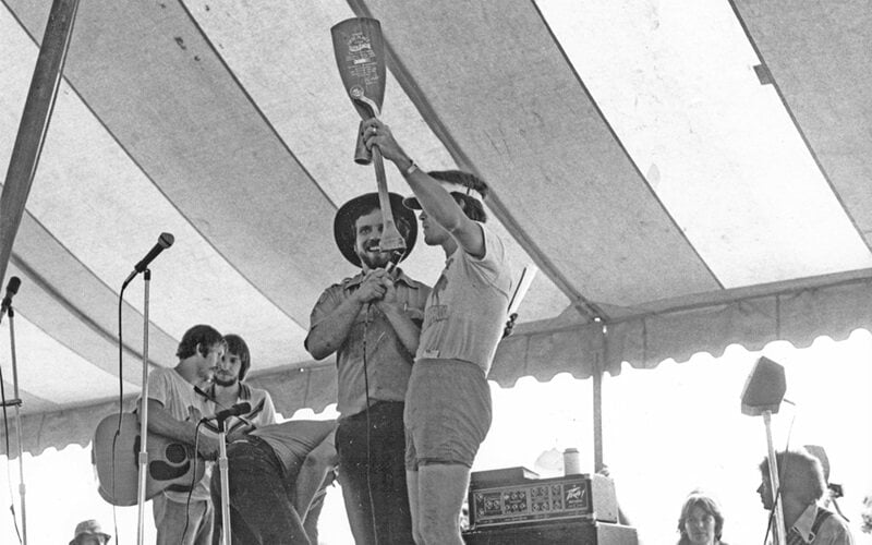 man with an boat paddle speaking on stage