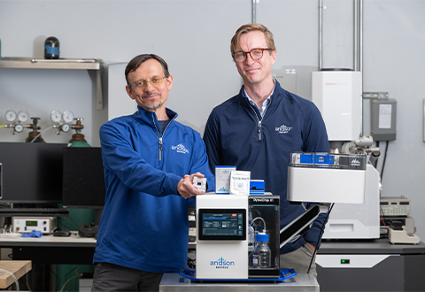Andrei Fedorov and Mason Chilmonczyk stand in a lab behind a device that says Andson Biotech.