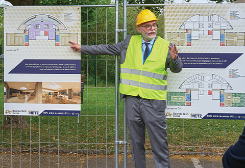 Georgia Tech-Europe President Abdallah Ougazzaden wearing a hard hat and construction vest standing in front of a fence that shows plans for the renovation. 