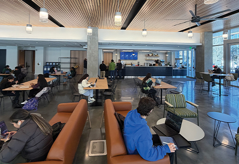 several couches inside a main lobby with concrete floors and bright lighting. A coffee shop is in the background. 