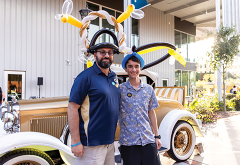 A man and boy wearing balloon hats posed in front of the Ramblin' Wreck.