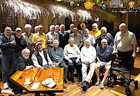 A group of TKE alumni pose in front of a tiki bar setting. 