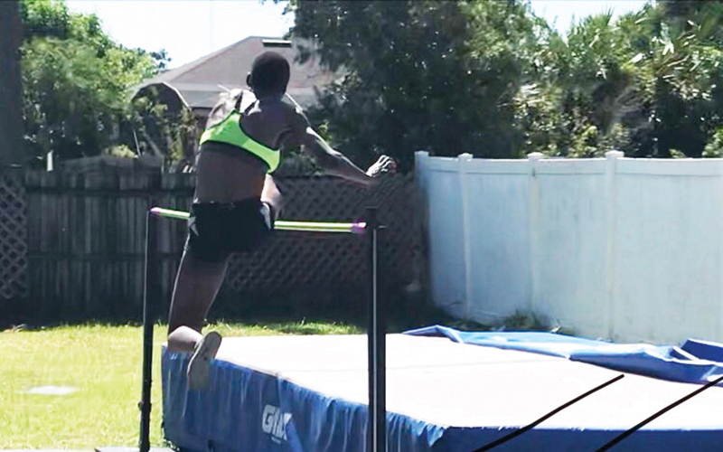 A high-angle photo shows a woman clearing a high jump bar and about to land on a blue mat.