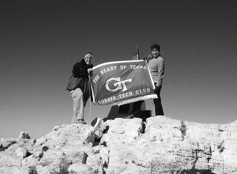 Black and white photo of two people holding a "Georgia Tech Club" flag on a rocky mountain summit.