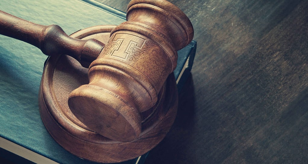 A high-angle, close-up shot of a wooden gavel resting on top of a dark blue legal book.