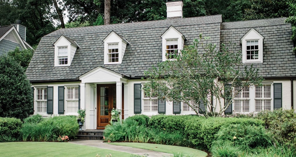 A two-story, white house with a dark gray shingled roof, dark green shutters, and a well-kept front yard.