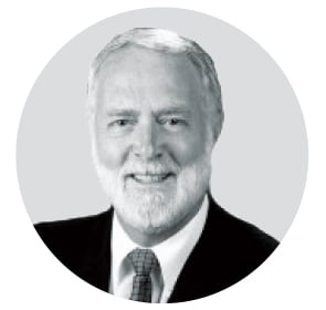 A black-and-white portrait of a bearded man, smiling in a suit and tie.